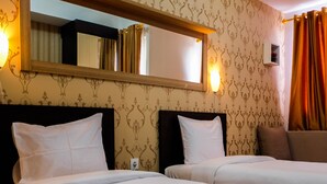 A hotel room with two beds, a large mirror above the beds, and a small shelf with a plant.