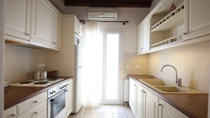A narrow kitchen with white cabinets, a wooden countertop, a built-in oven, and a sink with a faucet. - Villa Attalus 2 (Mykonos)