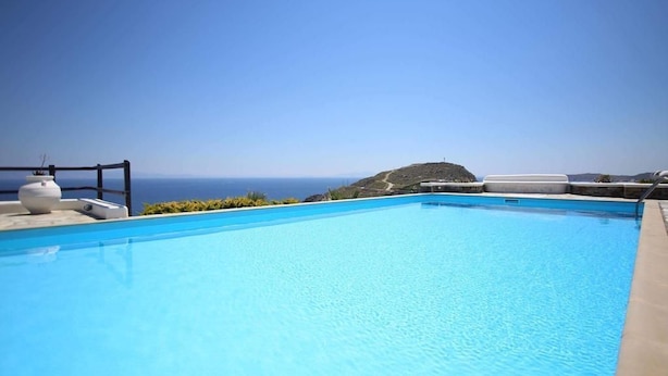 A clear blue swimming pool with a view of the ocean and a distant hill. - Villa Attalus 2 (Mykonos)