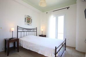 A bedroom with a single bed, two bedside tables, a nightstand, a ceiling light, a window with curtains, and a framed picture on the wall.
