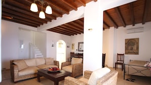 A cozy living room with wicker furniture, a coffee table, and a dining area with a chair and table. - Villa Attalus 2 (Mykonos)