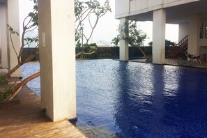 A swimming pool with a wooden deck and a view of a cityscape in the background. - Prime Location Studio Apartment at Elpis Residence near Ancol (Jakarta)