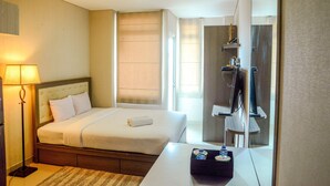A hotel room with a bed, bedside table, lamp, and a mirror reflecting the room. - Prime Location Studio Apartment at Elpis Residence near Ancol (Jakarta)