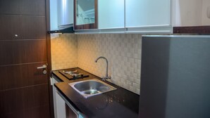 A compact kitchen with a stainless steel sink, a microwave, and a built-in oven. - Fully Furnished Studio Apartment @ The Enviro (Cikarang)