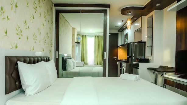 A hotel room with a large bed, a television, a desk, and a bathroom visible through an open door. - Fully Furnished Studio Apartment @ The Enviro (Cikarang)