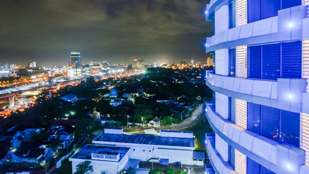 A modern building with multiple floors and balconies, surrounded by a cityscape with visible roads and buildings.