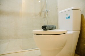 Des toilettes avec une serviette posée sur le couvercle, un espace douche et un filtre à eau fixé au mur.