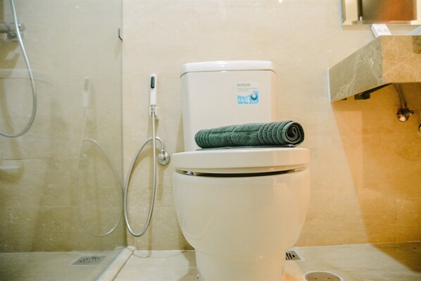 A bathroom with a toilet, a shower, and a towel on the toilet seat.