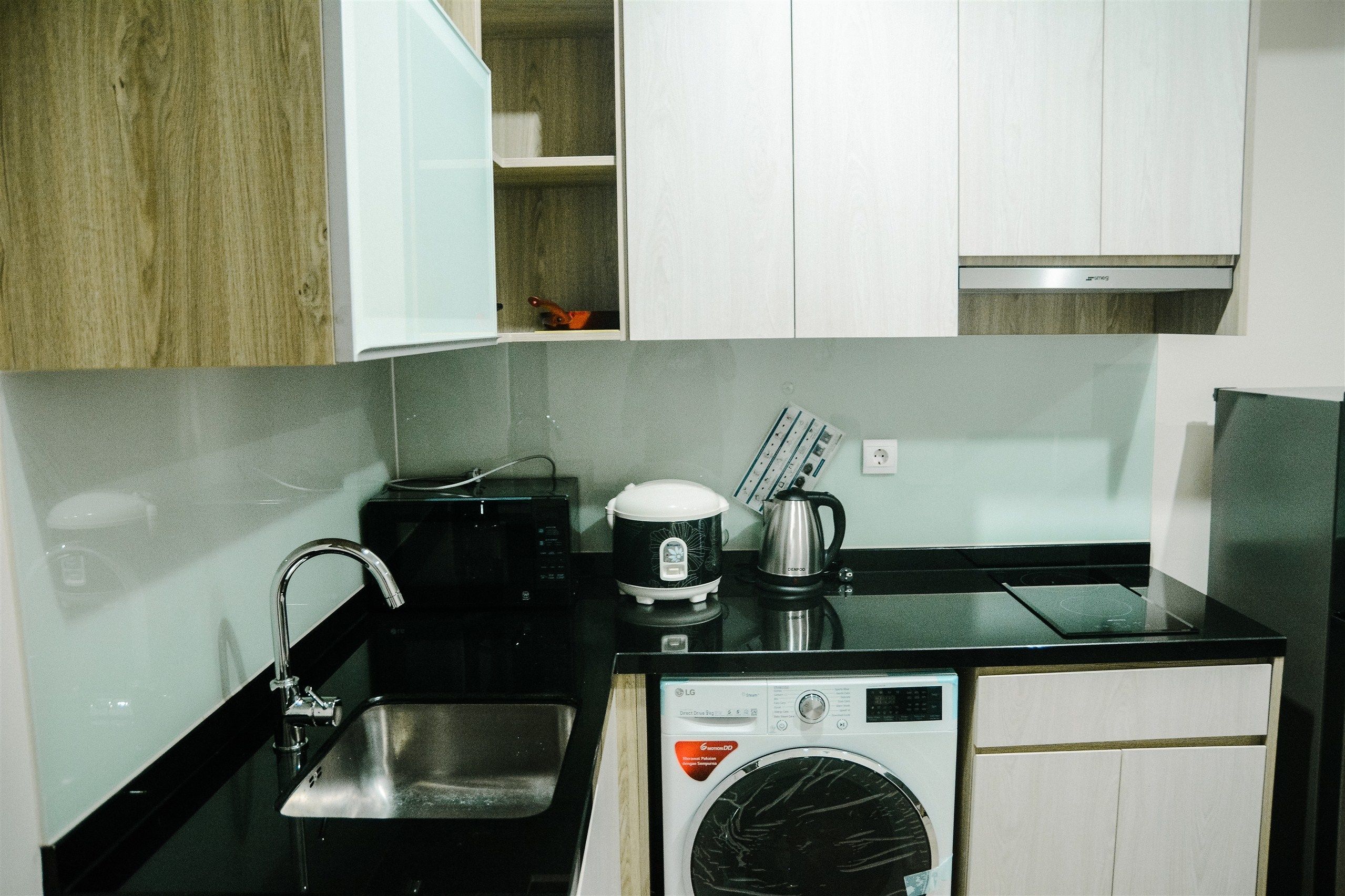 A compact kitchenette with a sink, a coffee maker, a microwave, and a compact washer-dryer unit.