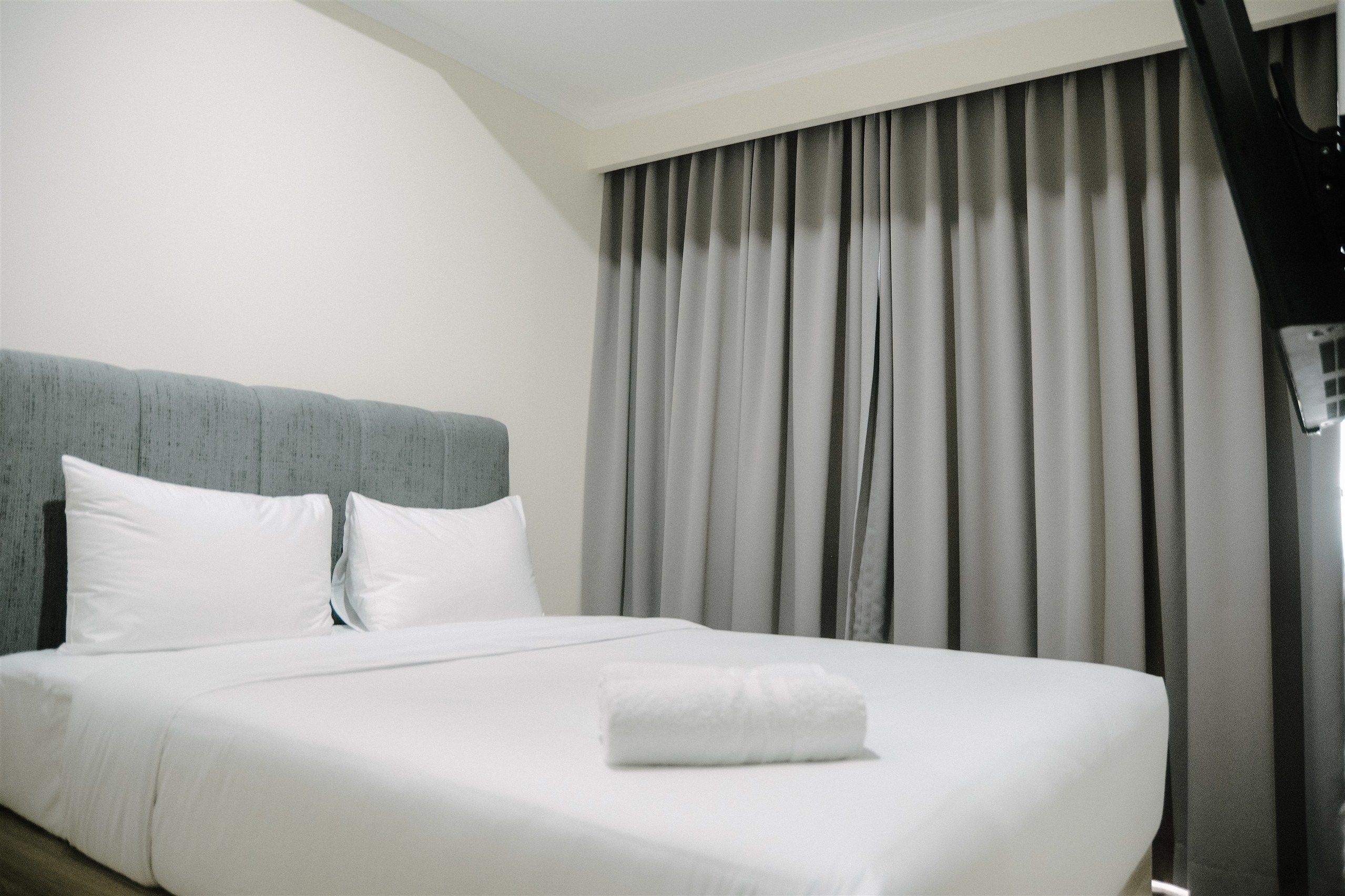 A hotel room with a neatly made bed, grey curtains, and a modern headboard.