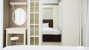 Une chambre avec une coiffeuse blanche, un miroir rond, un lit avec du linge de lit blanc et une tête de lit en bois.