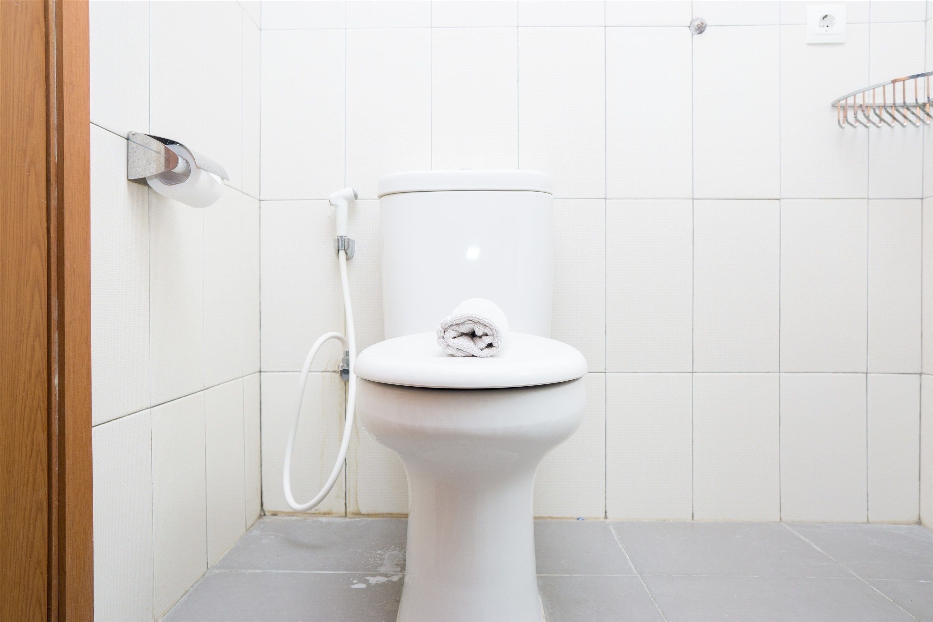 Inodoro blanco con una toalla sobre el asiento, una manguera de ducha y un perchero en la pared.
