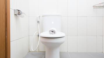 Inodoro blanco con una toalla sobre el asiento, una manguera de ducha y un perchero en la pared.