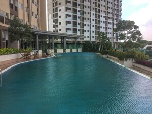En swimmingpool med et loungeområde, omgivet af en moderne bygning med flere etager og altaner.