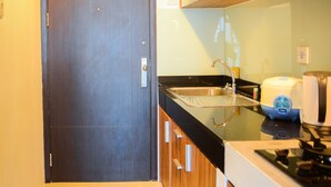A compact kitchen with a dark wooden door, a stainless steel sink, and a coffee maker on the counter. - Simply Homey Studio Room at GP Plaza Apartment (Jakarta)