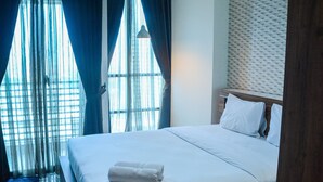 A hotel room with a large bed, a wooden headboard, and sheer curtains on the windows. - Simply Homey Studio Room at GP Plaza Apartment (Jakarta)
