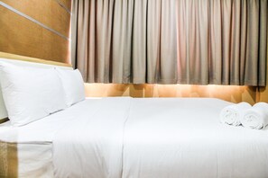A neatly made bed with white linens, a headboard, and a curtain.