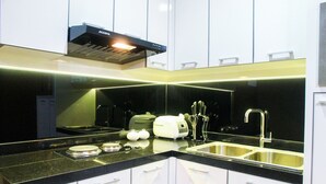 A modern kitchen with white cabinets, a black countertop, a built-in oven, a sink, and a range hood. - Cozy and Minimalist 1BR @ Oasis Apartment (Cikarang)