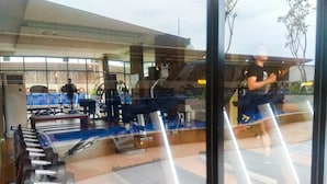 A gym with exercise equipment, a treadmill, and a mirrored wall reflecting a person running. - Studio Room Azalea Suites Apartment (Cikarang)