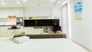 A modern hotel room with a kitchenette, a sofa, a TV, and a painting on the wall. - Studio Room Azalea Suites Apartment (Cikarang)
