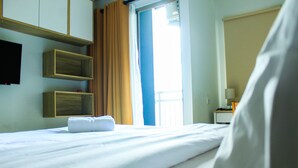 A hotel room with a bed, a window with curtains, a flat-screen TV mounted on the wall, and a bedside table with a lamp. - Modern and Comfortable Studio Springwood Apartment (Tangerang)