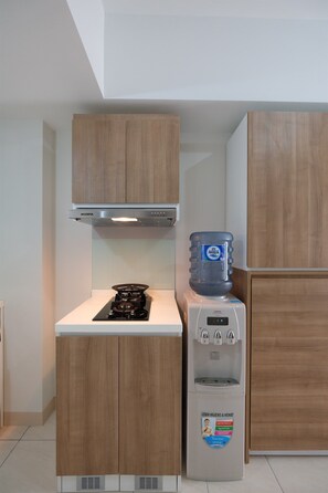 Une cuisine de taille réduite, équipée d’une cuisinière à gaz, d’un distributeur d’eau et de meubles de rangement en bois.