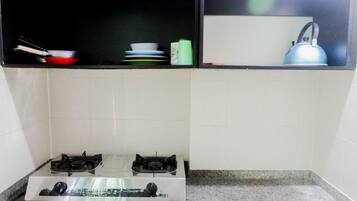 A kitchen with two gas stoves, a countertop, and a shelf above holding various kitchenware.