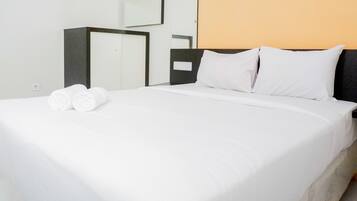 Una cama bien hecha con sábanas blancas y dos toallas enrolladas, un cabecero oscuro y un espejo fijado a la pared.
