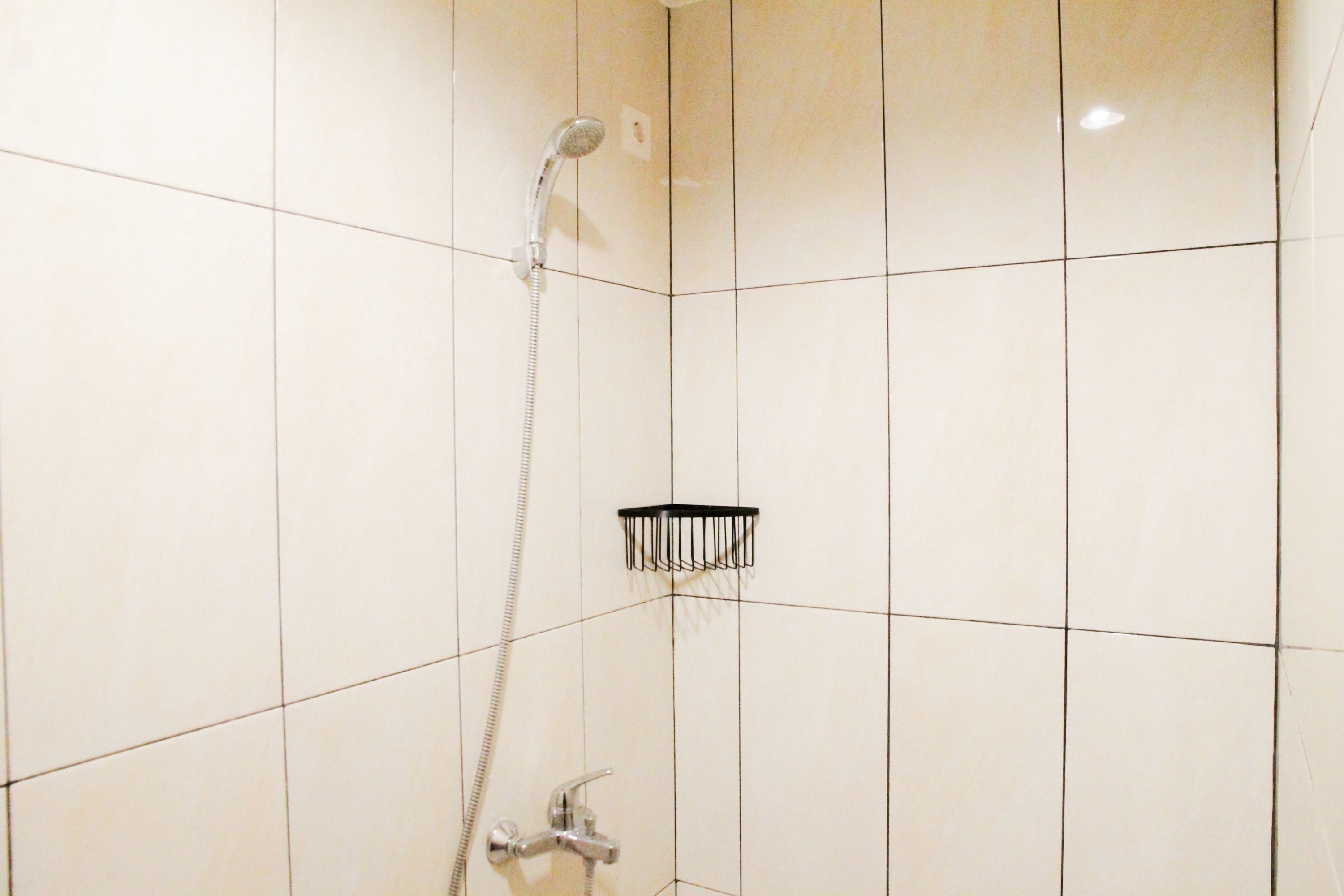 Un baño con paredes de azulejos blancos, una ducha con cabezal de mano y un cabezal de ducha negro en la pared.