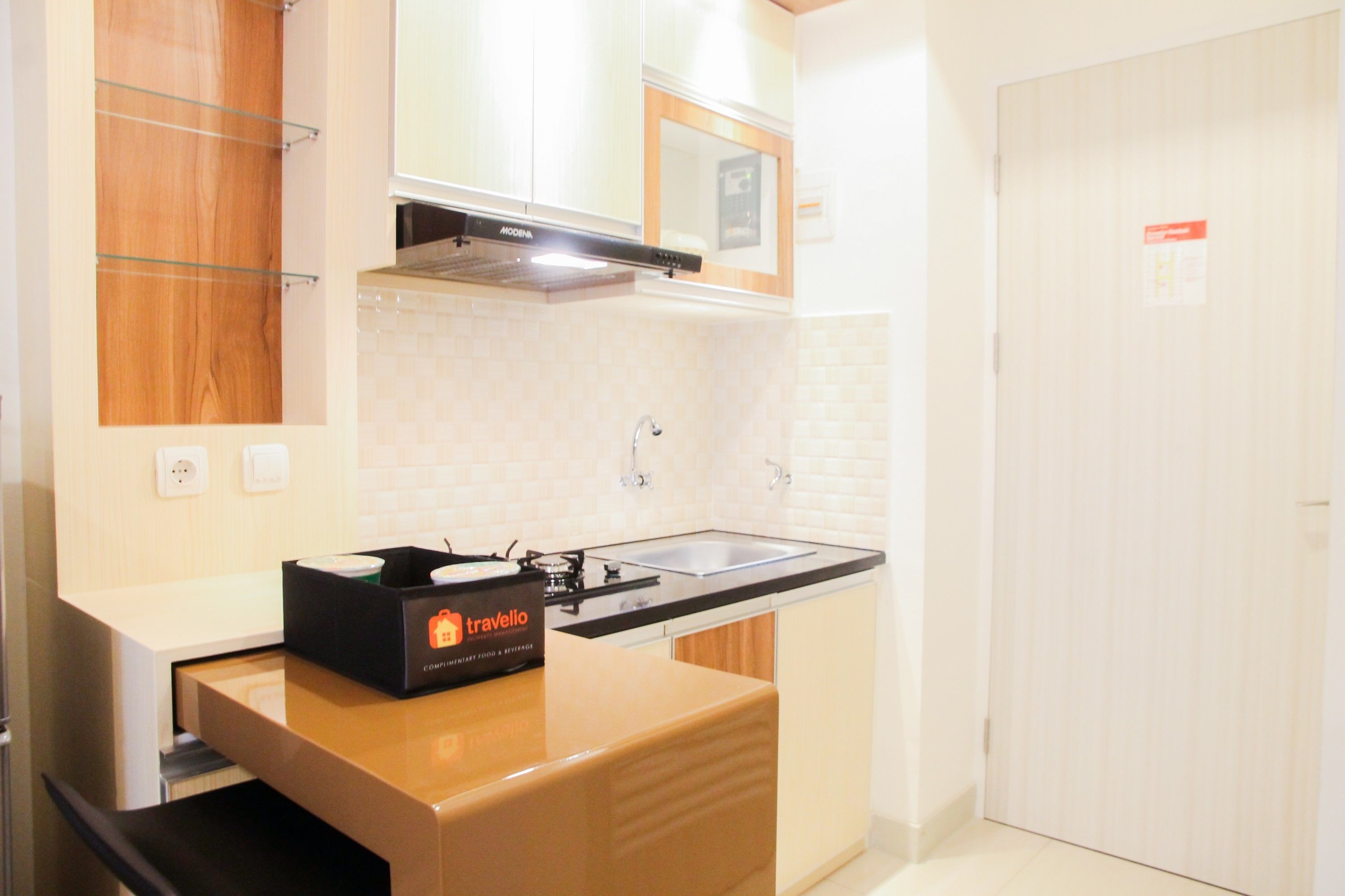 A compact kitchen with a sink, a microwave, and a travel bag on the counter.