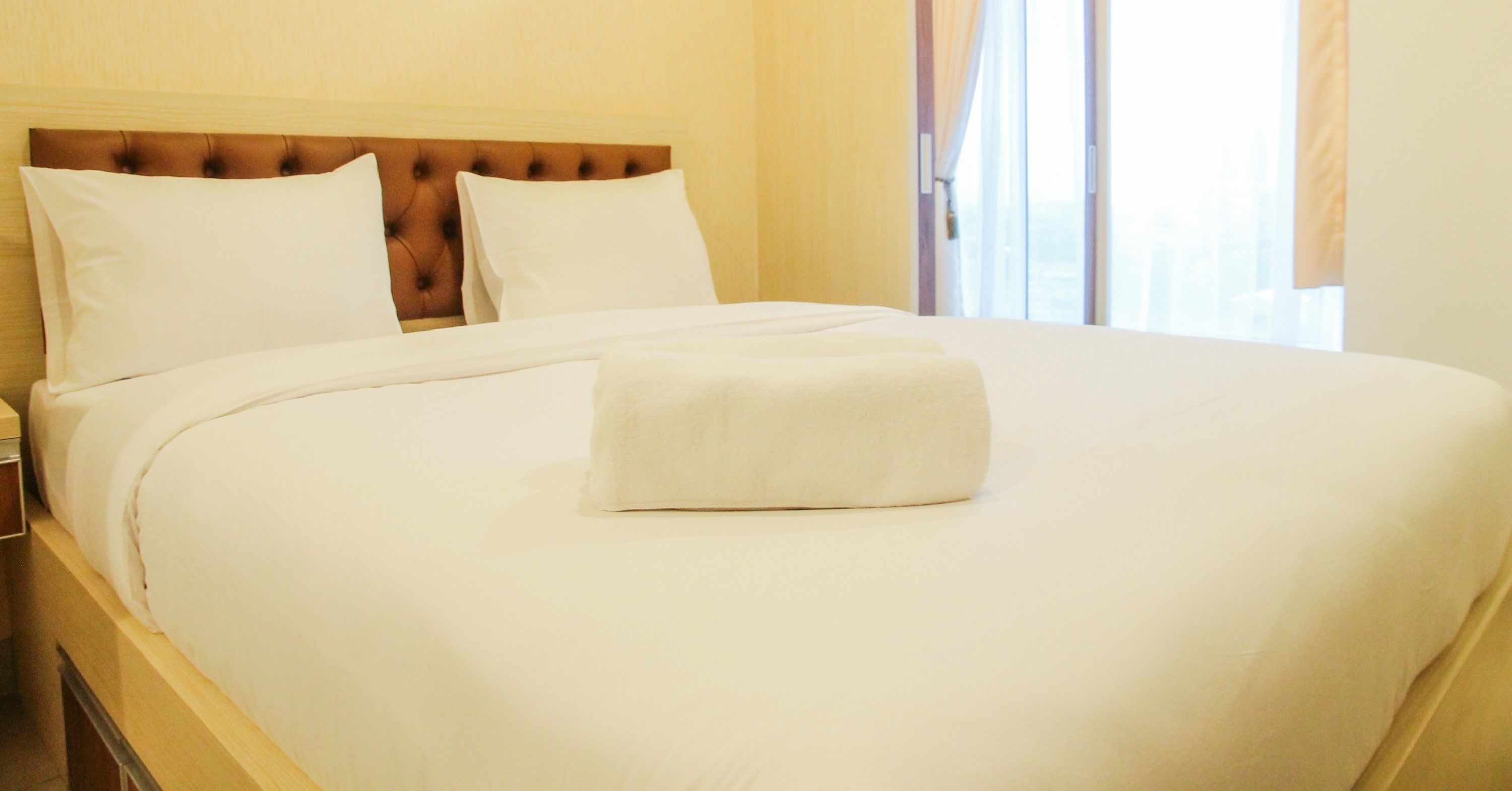 Un lit bien fait, avec du linge de lit blanc et une tête de lit marron, dans une chambre d’hôtel.