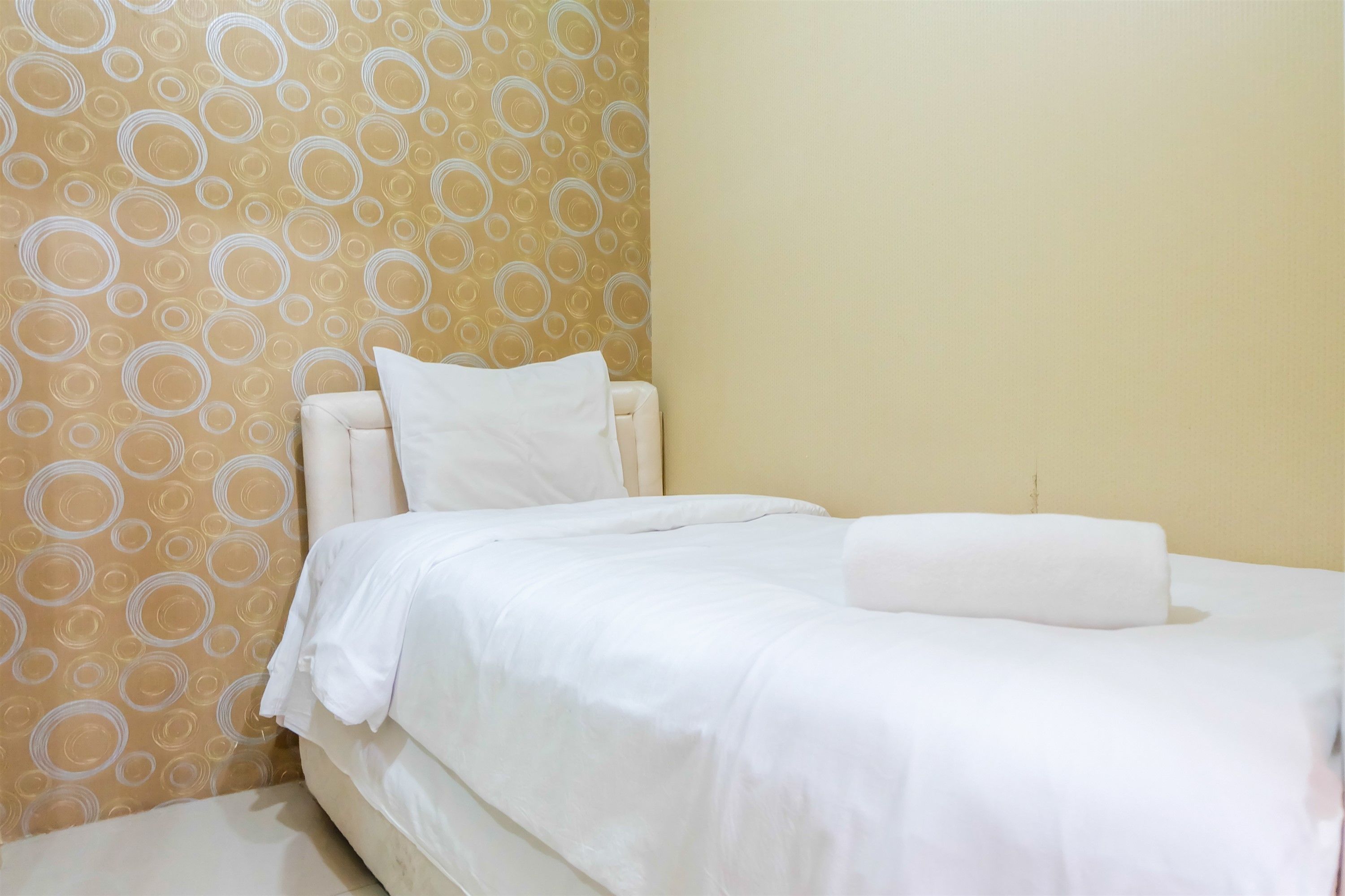 A neatly made bed with white linens in a room with a patterned wallpaper and a plain wall.