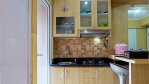 A compact kitchen with wooden cabinets, a stainless steel sink, and a built-in range hood. - Affordable Price 2BR Green Pramuka City Apartment (Jakarta)