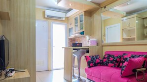 A modern kitchen with wooden cabinets, a pink sofa with floral cushions, and a bar stool. - Affordable Price 2BR Green Pramuka City Apartment (Jakarta)