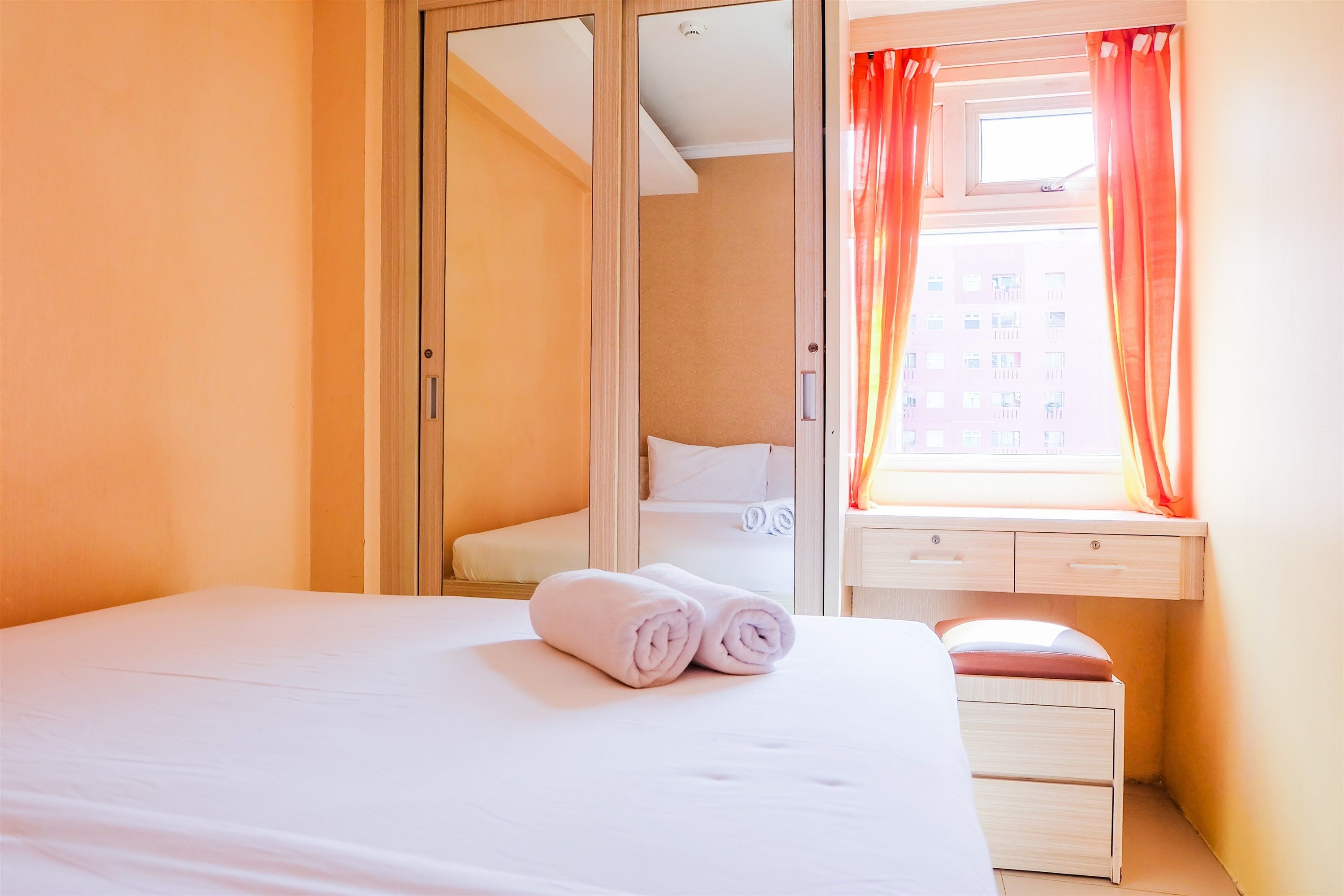 A hotel room with a bed, a window with curtains, a desk, and a mirror.