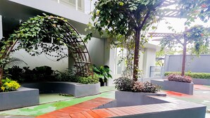 A courtyard with a wooden deck, planters with various plants, and a pergola covered in greenery. - Simply Homey Studio Casa De Parco Apartment (Pagedangan)