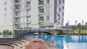A modern apartment building with a swimming pool, a wooden deck, and a bridge connecting different levels. - Simply Homey Studio Casa De Parco Apartment (Pagedangan)