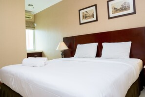 Quarto de hotel com uma cama grande, mesa de cabeceira com abajur e duas molduras na parede.