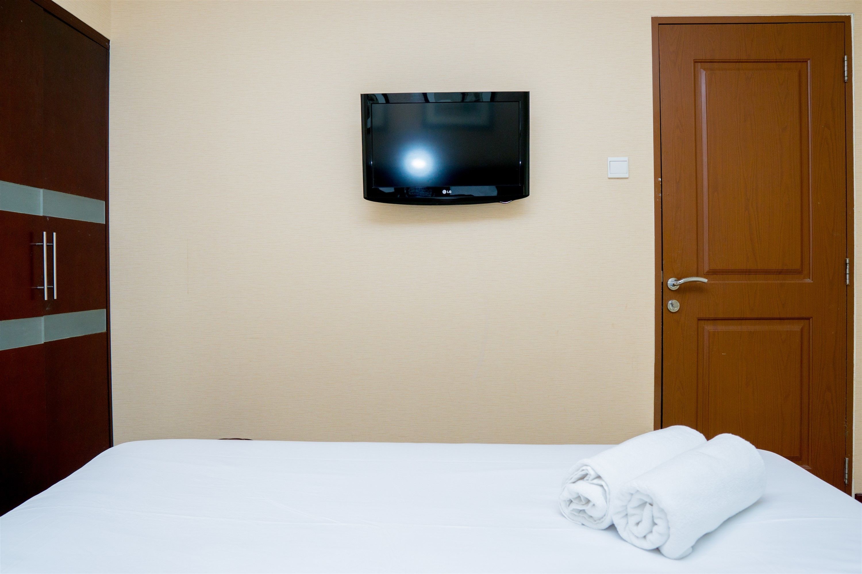 Una habitación de hotel con una cama, un televisor montado en la pared y una puerta de madera.