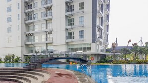 A modern apartment building with a swimming pool, a wooden deck, and a bridge over the pool. - Nice & Comfy Studio Apartment Casa De Parco (Pagedangan)
