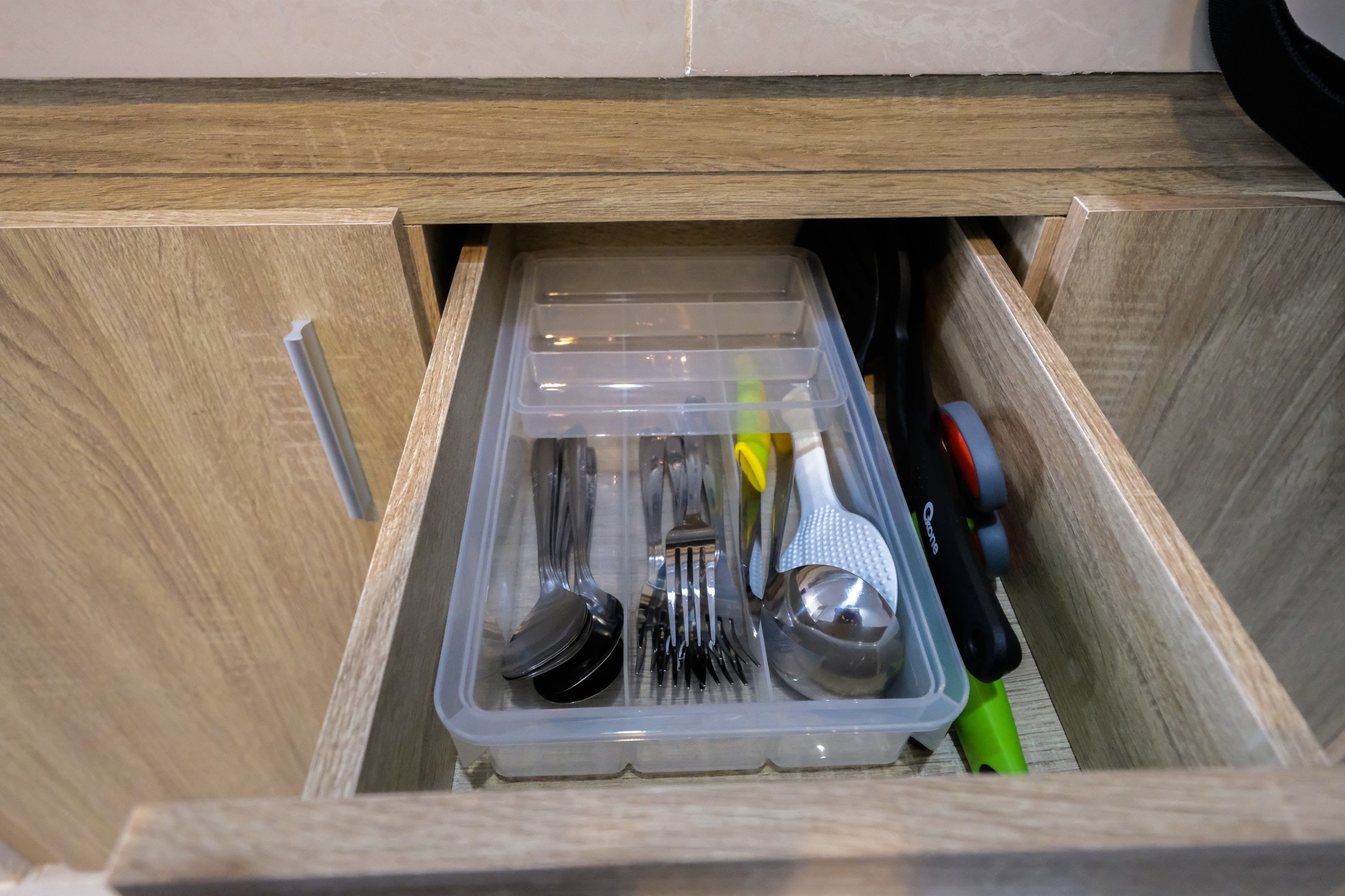 A drawer with a clear plastic organizer containing utensils and a grater.