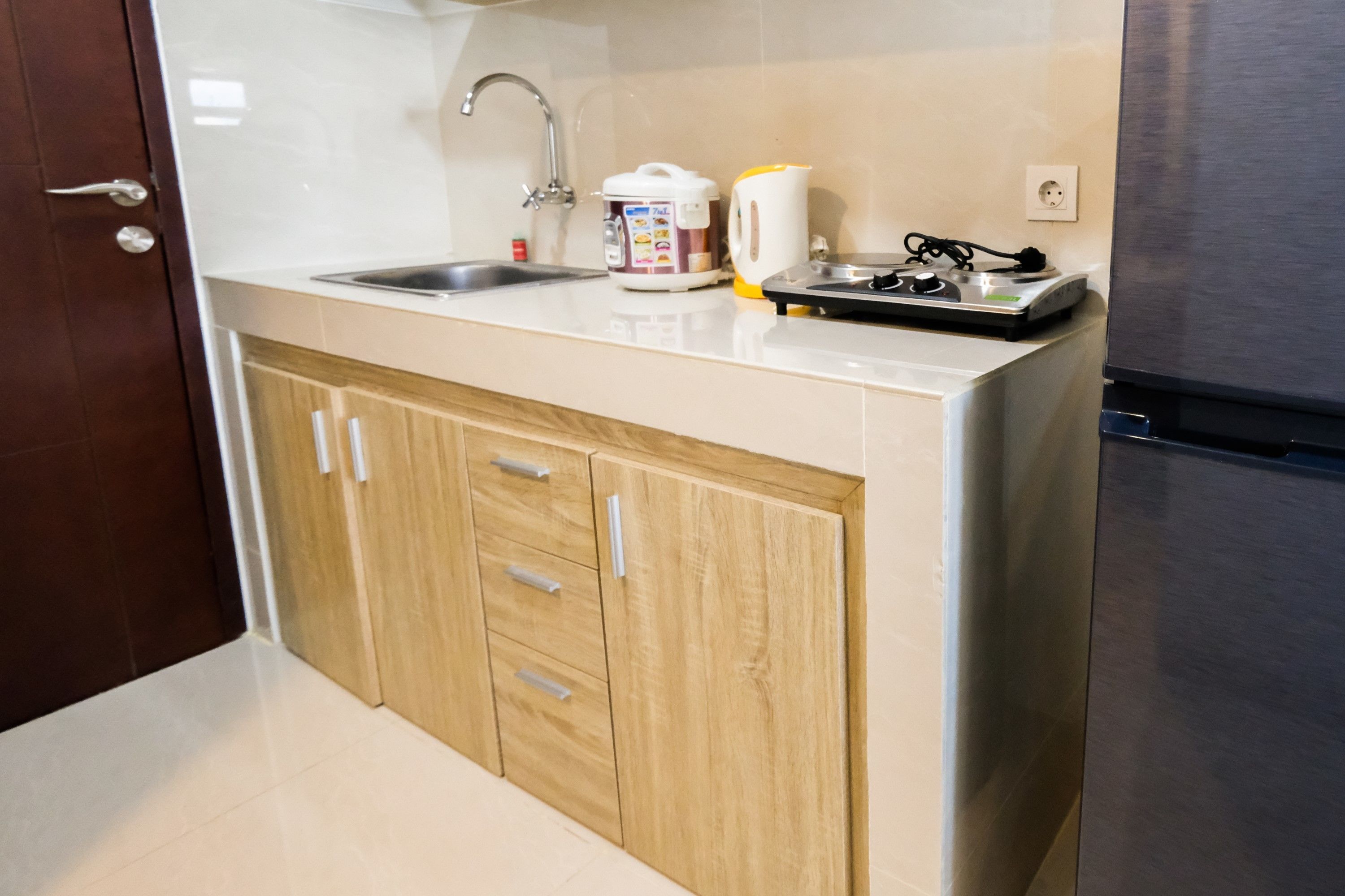 A kitchen with a sink, wooden cabinets, a stainless steel refrigerator, and a coffee maker.