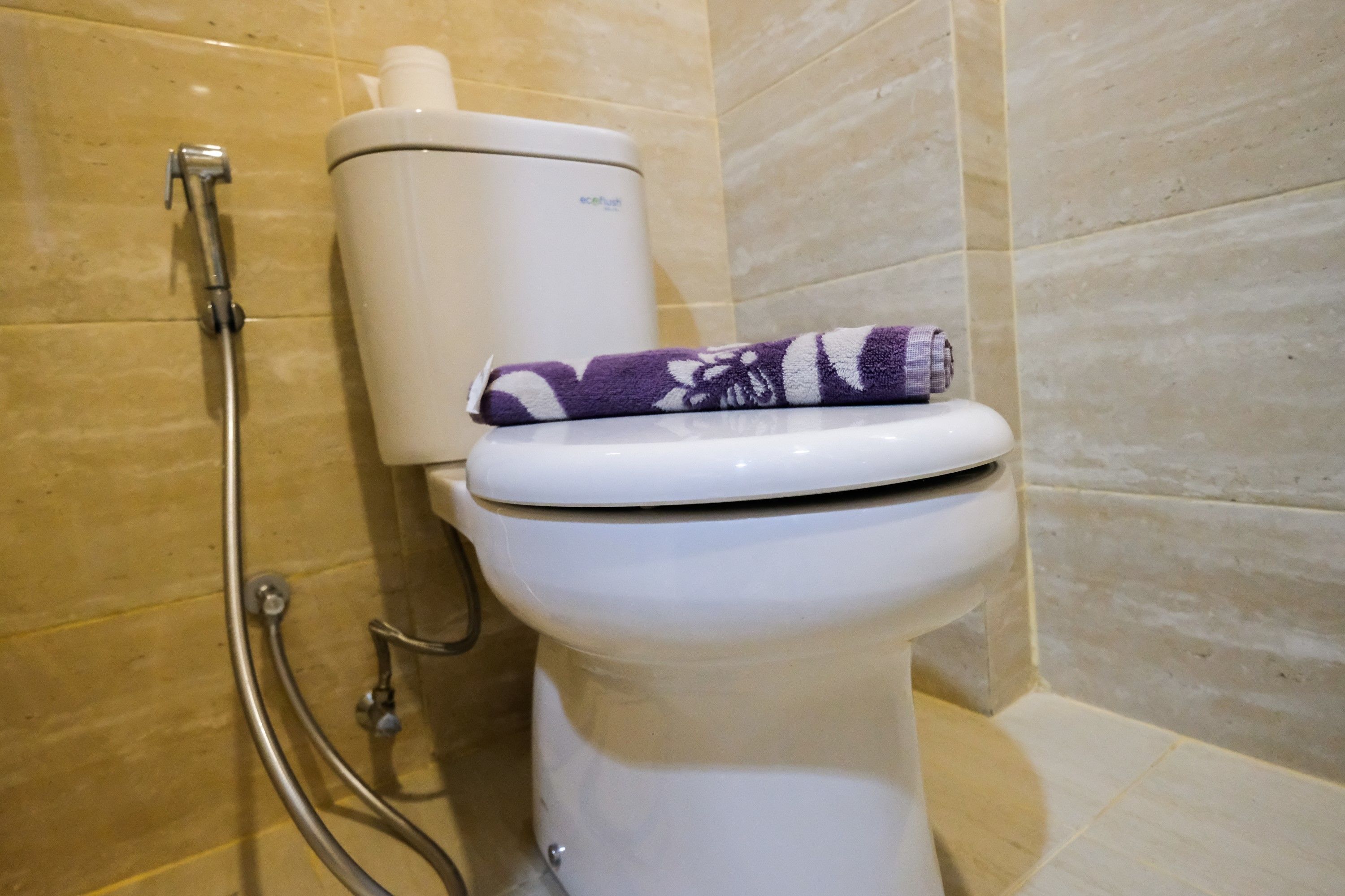 Eine Toilette mit einem weißen Tank und einem lila Handtuch auf dem Sitz.