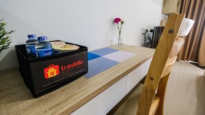 A hotel room with a wooden desk, a black bag labeled 'travelio', and a vase with flowers. - Exclusive Studio Apartment Springwood Residence (Tangerang)