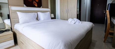 Una cama bien hecha con sábanas blancas y toallas enrolladas, un cabecero de madera y un espejo grande encima.