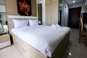 A neatly made bed with white linens and rolled towels, a wooden headboard, and a large mirror above it. - Exclusive Studio Apartment Springwood Residence (Tangerang)