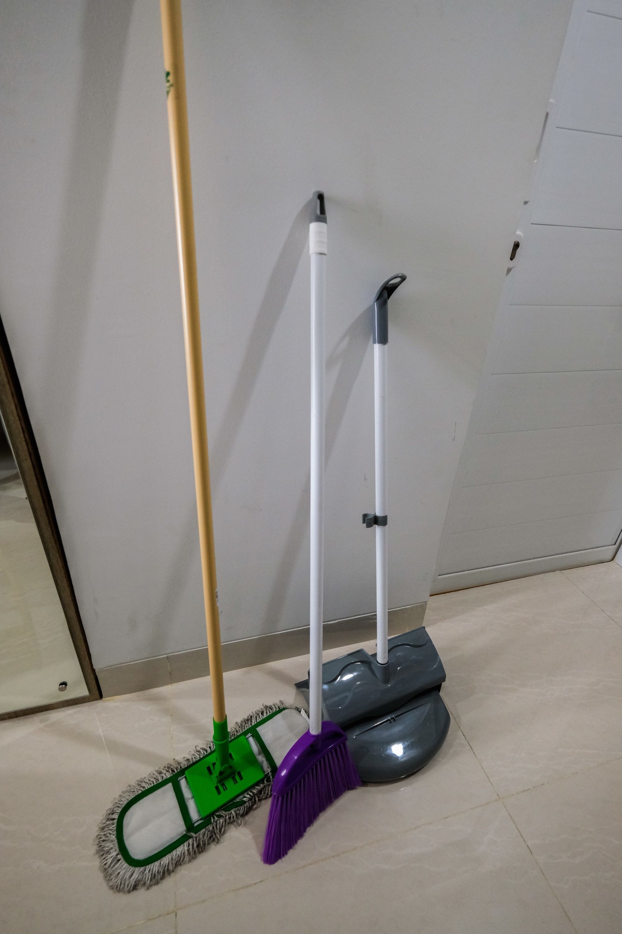 A mop and broom leaning against a wall in a room with tiled flooring.