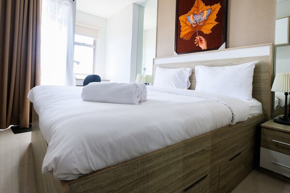 A neatly made bed with white linens, a wooden headboard, and a bedside table with a lamp. - Exclusive Studio Apartment Springwood Residence (Tangerang)