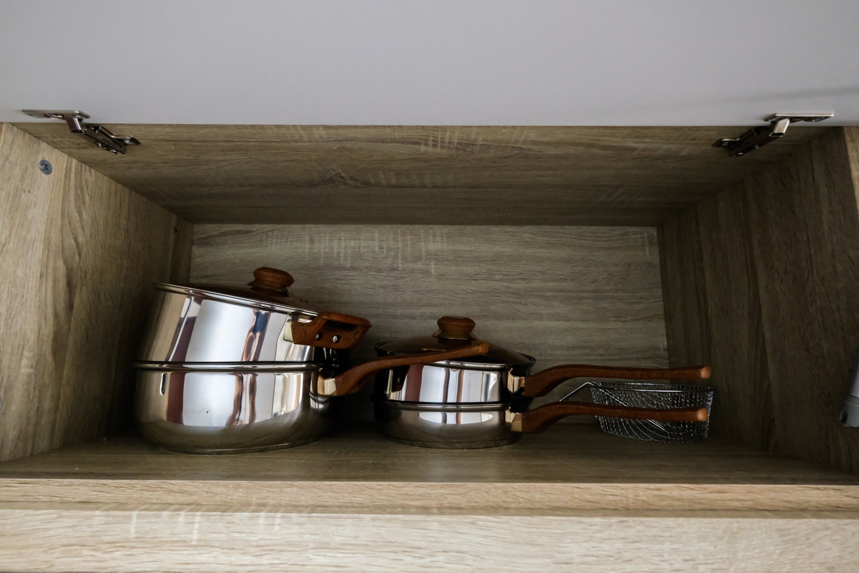 Un mueble de madera con tres ollas y tapas de acero inoxidable, y un colador de metal.