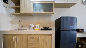A kitchen with wooden cabinets, a black refrigerator, a coffee maker, and a kettle. - Exclusive Studio Apartment Springwood Residence (Tangerang)